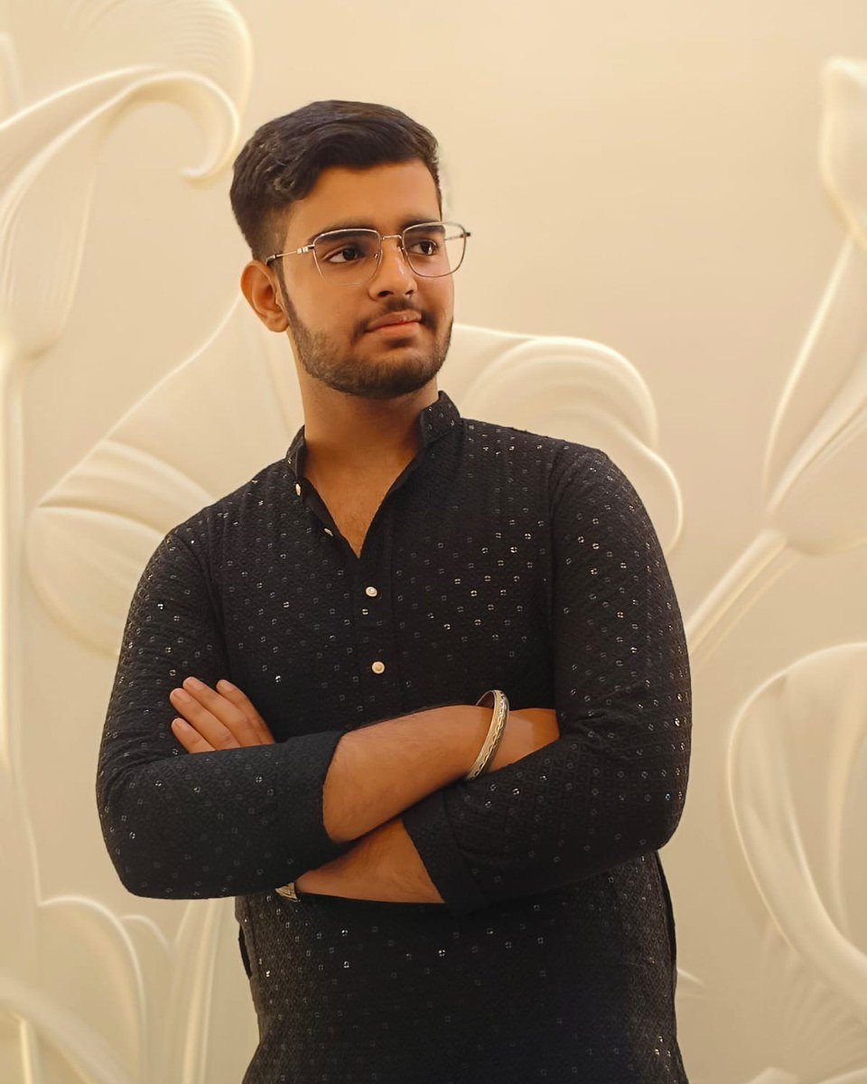 Aman Lakhwani in a black embroidered kurta, arms crossed, in front of a carved ivory wall